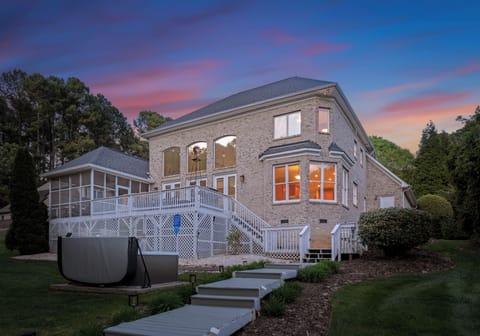 Beautiful brick home with a spacious deck, screened porch, and a glowing sunset backdrop.