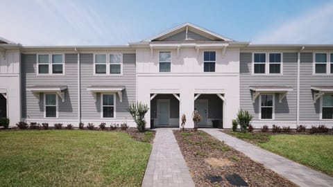Experience a charming exterior featuring a modern design with light gray siding and white accents. The inviting entrance, surrounded by beautifully landscaped pathways and greenery, warmly welcomes you for a delightful stay.