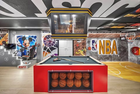 Enter a lively game room celebrating basketball culture, highlighted by a striking red pool table and unique basketball display. Colorful murals and dynamic lighting set an energetic atmosphere, ideal for fun-filled evenings.