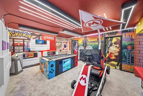 Discover a lively game room with bright red walls and playful decor, featuring a standout Mario Kart setup and colorful gaming stations, making it the ideal spot for fun-filled evenings with family and friends.
