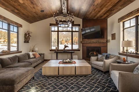 Cozy up in your rustic-chic living room with vaulted wood ceilings, where plush seating surrounds a warm fireplace and snowy mountain views frame perfect winter evenings.