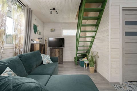A bright living room with a green sofa and a staircase leading upstairs. The space feels open and modern.