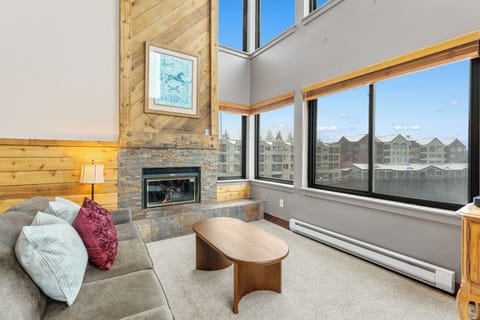 Unwind in your bright living room with soaring ceilings, a cozy stone fireplace, and windows framing resort views—your perfect mountain retreat.