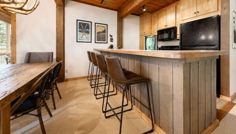 Your cozy mountain retreat features rustic wood accents, a welcoming kitchen bar perfect for morning coffee, and a spacious dining table where you can gather and share stories after a day of adventure.