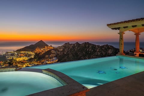 Stunning infinity pool overlooks coastal mountains and city lights during golden sunset. Perfect evening setting with hot tub.