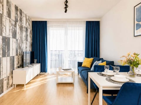 The living room is anchored by a deep blue sofa with yellow accent pillows, set against a wall with textured grey paneling. A white coffee table and media console complete the modern, airy aesthetic.
