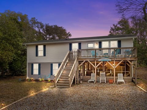 Charming coastal retreat with wraparound deck and covered outdoor seating, nestled among mature trees for the perfect getaway.