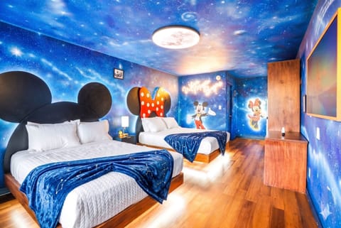 This themed bedroom features two beds with mickey and minnie mouse headboards and a galaxy-inspired ceiling and walls for a playful stay.