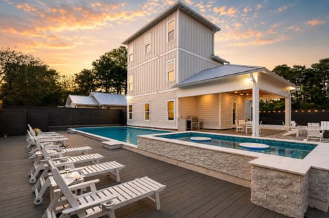 Evening view of the modern multi-story exterior with an illuminated private pool and lounge area.