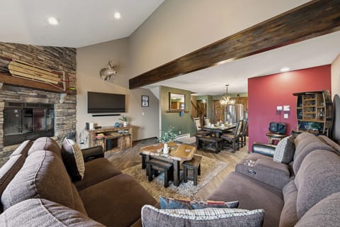 Warm, cabin‑style living and dining area with a cozy sectional, stone fireplace, and inviting wood‑beam charm.