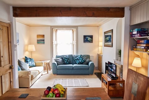 Sunny open-plan living with two sofas, games and coastal art throughout.