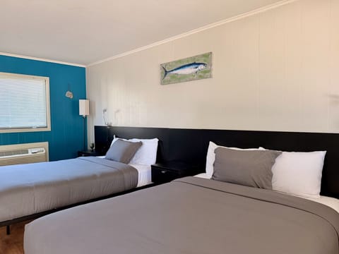 Two queen beds with plush dark headboards, teal accent wall, and metal fish wall art