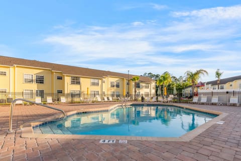Outdoor pool area with lounge chairs and yellow residential buildings under a clear sky