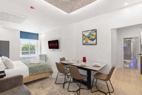 A beautifully designed open-plan space featuring a plush double bed, elegant dining area and Smart TV. Large windows fill the room with natural light, while the modern layout creates a bright, stylish and relaxing hotel-style retreat.