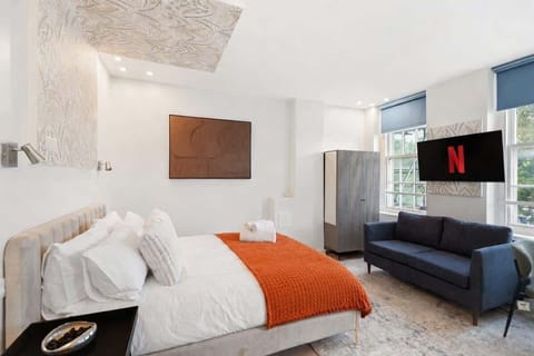 A bright, boutique-style bedroom with a luxurious double bed, stylish sofa and Smart TV with Netflix. Large windows fill the space with natural light, creating a calm, elegant retreat perfect for relaxing after a day in the city.
