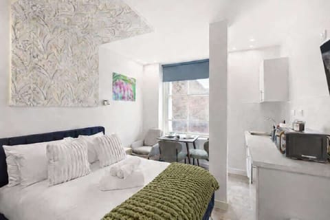 A bright, boutique-style bedroom with a luxurious double bed, stylish sofa and Smart TV with Netflix. Large windows fill the space with natural light, creating a calm, elegant retreat perfect for relaxing after a day in the city.