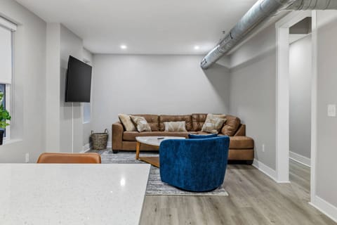 Living area viewed from the kitchen island, showing the leather sectional, blue accent chair, Smart TV, and hallway.