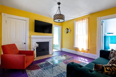 Sun-filled living room with 65-inch Smart TV, teal velvet sofa, and a glass chess set on the coffee table.