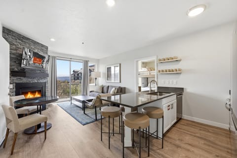 Bright open-concept living room and kitchen with fireplace, bar seating, and mountain views from large windows