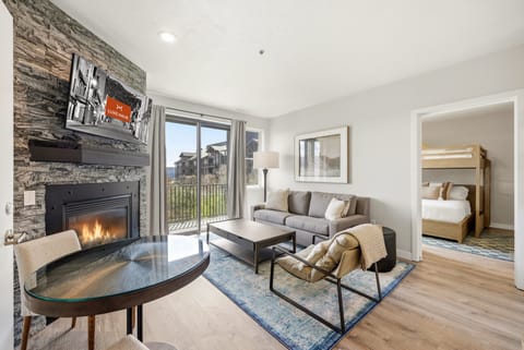 Cozy living area with stone fireplace, large windows, and adjacent bunk room, filled with natural light