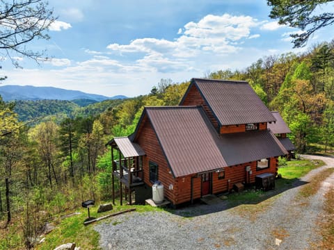 Hillside log cabin surrounded by lush forest, with wide mountain views and a peaceful blue‑sky backdrop.