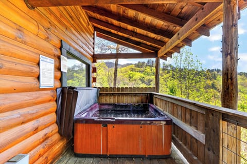 Covered cabin deck with a private hot tub, timber beams, and wide open views of the forested hills.
