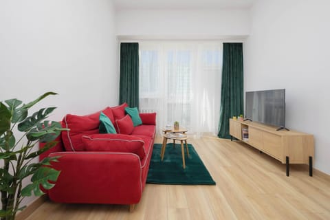 A cozy seating area centered around a red couch and a dark green rug, complemented by simple wooden furniture.