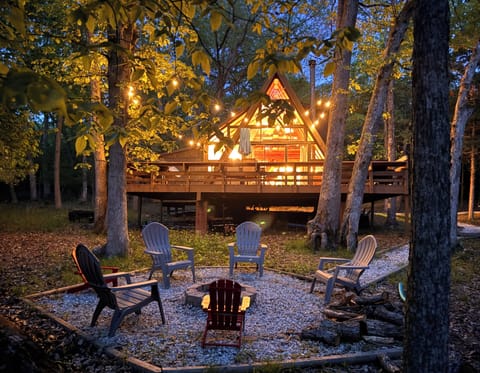 Cozy A-frame cabin in woods with deck, string lights, and fire pit seating