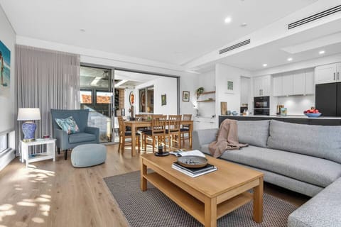 Settle into the light-filled living area, where a plush sofa, armchair nook, and TV come together to create a calm, inviting space to unwind at any time of day.