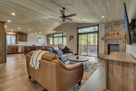 Sunlit living area w/ cozy seating, stone fireplace & large windows framing the forest outside