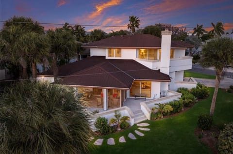Stunning two-story home surrounded by tropical palms and manicured gardens, showcasing modern architecture against a vibrant sunset sky.