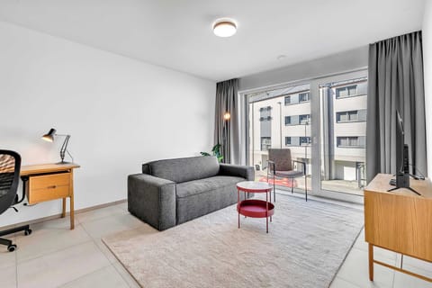 Bright living area with sofa, TV, and large windows bringing in natural light.