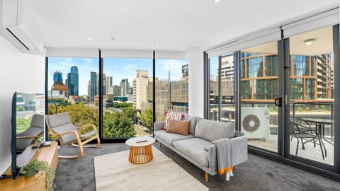 Light-filled lounge with floor-to-ceiling windows, comfy seating, and direct access to a private balcony with city views.
