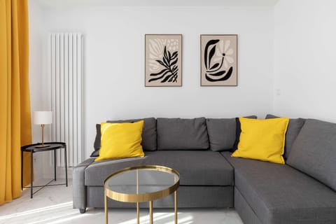 A modern living room with a gray sofa accented by bright yellow cushions, a small round coffee table, and minimalist wall art.