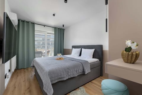 A modern bedroom with a neatly made bed, soft gray tones, and a small seating area near the window.