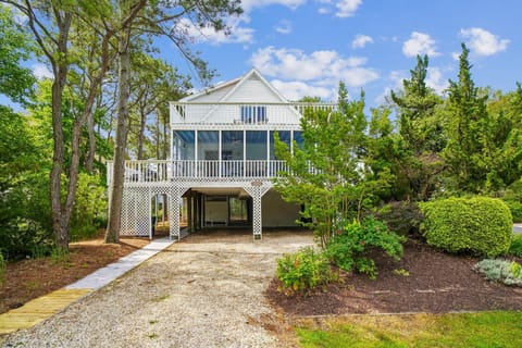 A charming coastal retreat nestled among mature trees with screened porches, elevated deck spaces, and covered parking surrounded by lush landscaped gardens.