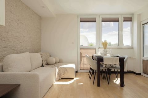 A well-lit seating area with a sofa positioned near the window and a small dining table in the center. Soft colors and clean lines make the room feel uncluttered and relaxing.