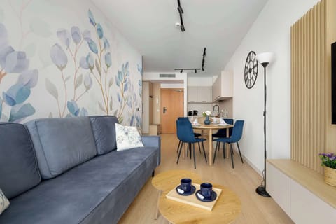 A modern living room with a grey sofa and a decorative feature wall with a botanical mural. The space opens into a dining area, creating a bright and cohesive layout.