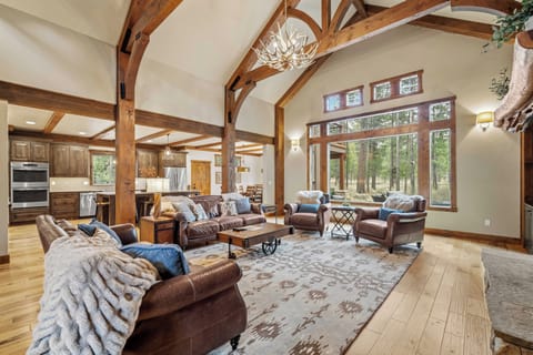 Unwind in this stunning great room with soaring timber beams, leather seating, and forest views streaming through floor-to-ceiling windows.