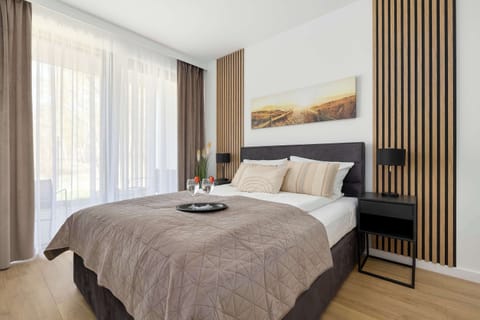 A serene bedroom with a double bed, soft beige tones, and large windows letting in natural light.