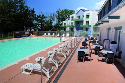 Pool terrace with white loungers on one side and outdoor café tables and chairs on the other, apartment building behind