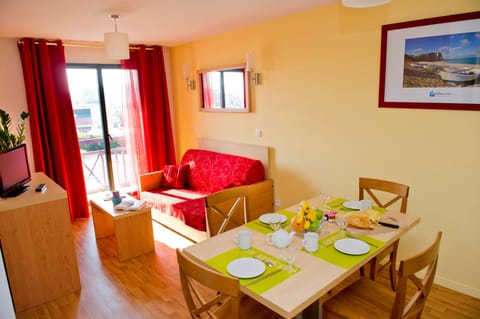Sunlight streams into the living area, highlighting the red sofa and wooden dining set