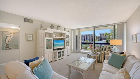 Living room with glass-top coffee table, white entertainment center, striped armchair, and sliding balcony doors.
