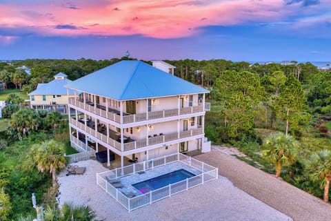 Aerial view of a coastal property nestled among lush tropical vegetation with a vibrant sunset painting the sky above.