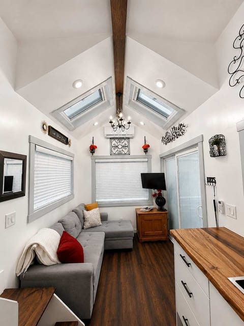 Bright living room with vaulted ceilings, skylights, and large windows. Cozy sectional converts to a sofa bed for extra sleeping space, plus smart TV and modern finishes in this thoughtfully designed tiny home.