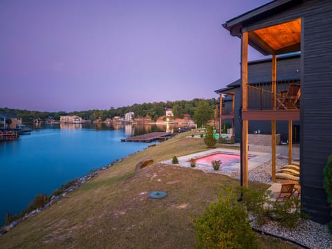 Multi-level covered balconies offering elevated views over the illuminated pool, manicured lawn, and water.