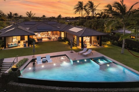 Luxury tropical estate featuring a stunning pool and hot tub, surrounded by swaying palms beneath a vibrant sunset sky.