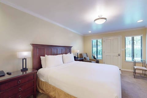 Settle into your plush king bed after a day exploring Napa Valley wineries — crisp white linens, elegant dark-wood furnishings, and soft lighting set the tone for a restful retreat.