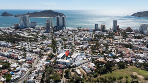 Aerial view highlights the apartment complex with a pool, surrounded by white buildings and ocean backdrop.