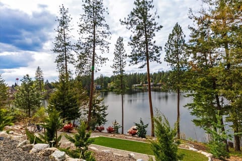 Elevated lake view with landscaped yard, dock, and pine-forest backdrop — the photo you'll screenshot before booking